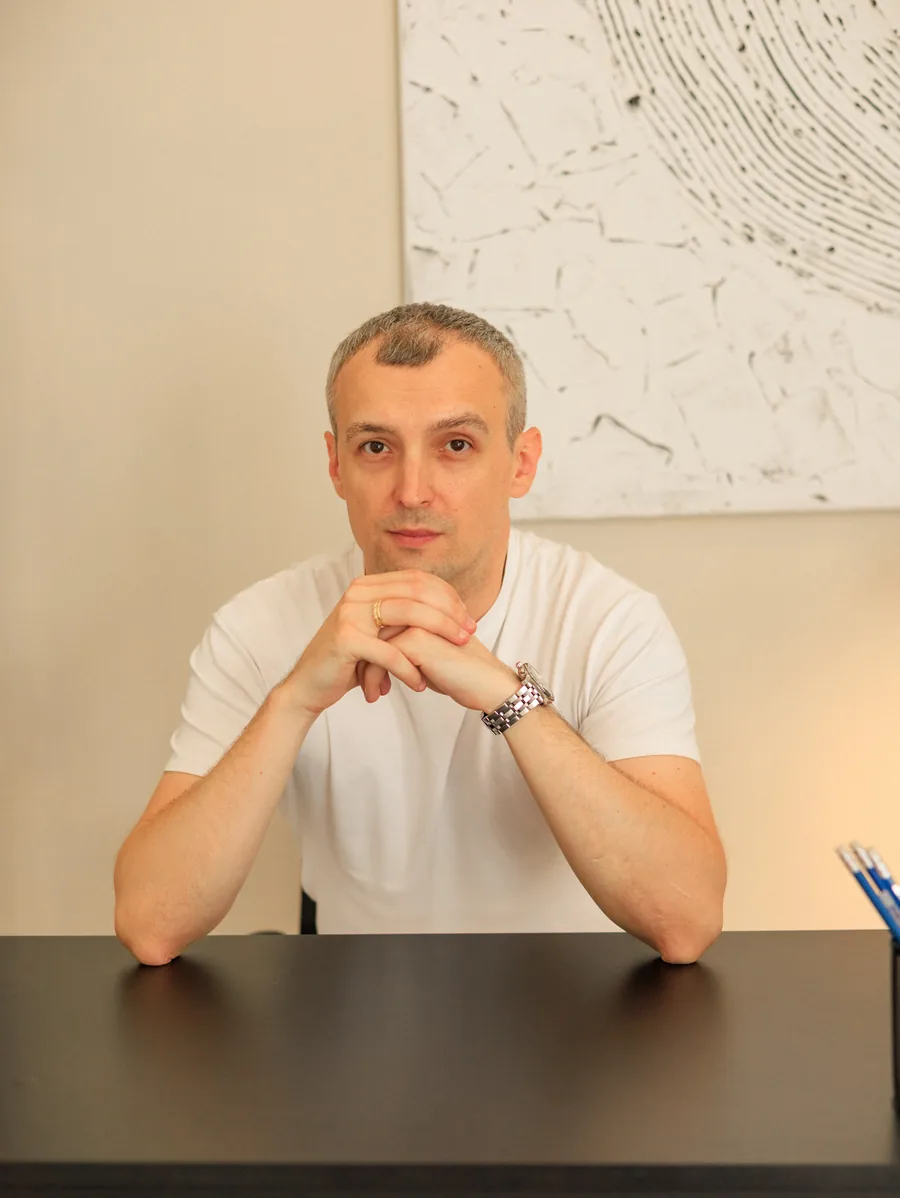 Yaroslav Volkov in a white T-shirt, seated at a desk with his hands together.