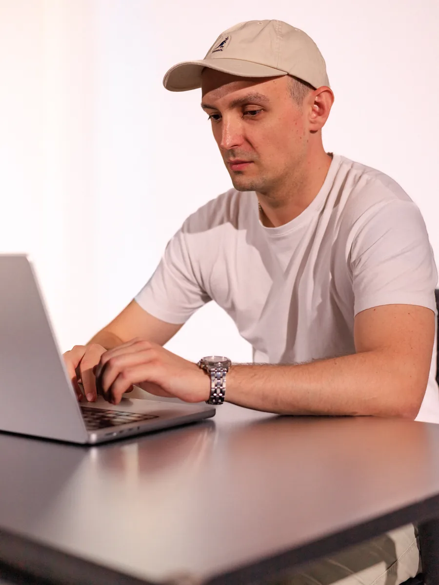Yaroslav Volkov wearing a cap and typing on a MacBook at a desk.