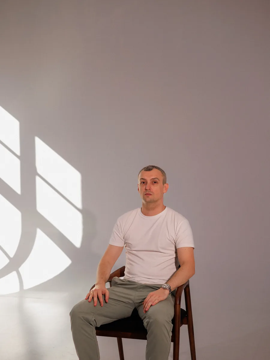 Yaroslav Volkov seated beside a pattern of window light on the studio wall.