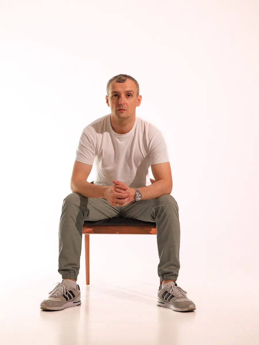 Yaroslav Volkov seated on a wooden chair in a white T-shirt and grey trousers.