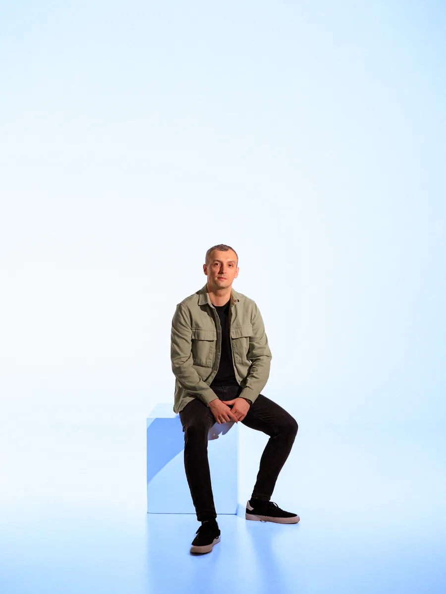 Yaroslav Volkov in a green overshirt, seated against a blue-lit studio backdrop.