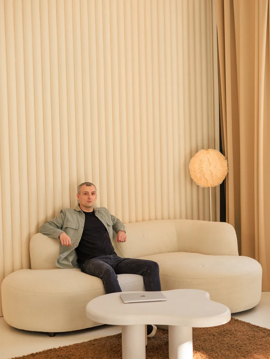 Yaroslav Volkov seated on a cream sofa beside a round lamp and curtains.